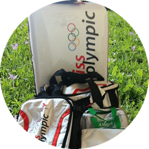 Mehrere Swiss Olympic Sporttaschen und ein grosser Koffer von Pack Easy stehen auf einer Schweizer Blumenwiese – ideales Reisegepäck für Schweizer Spitzensportlerinnen und -sportler.