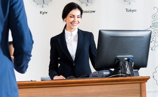 Hotel-Rezeptionistin mit Computer – Empfangssituation in internationalem Business-Hotel mit Weltzeituhren